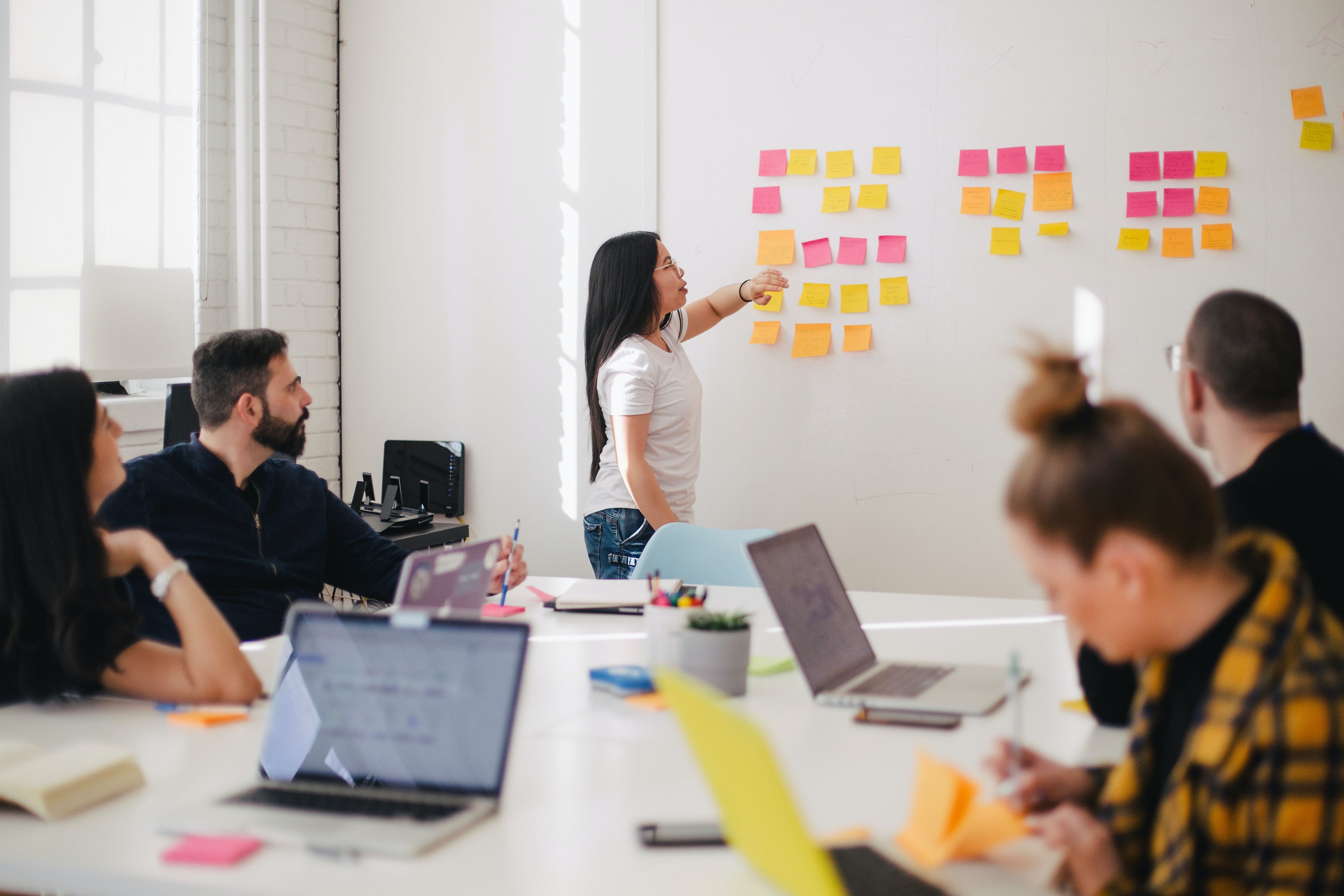 A presenter in a meeting looks at post-its hanging against the wall that are the result of a brainstorming session.