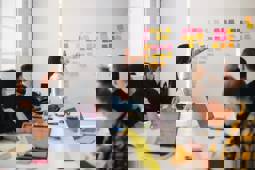 A presenter in a meeting looks at post-its hanging against the wall that are the result of a brainstorming session.