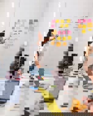 A presenter in a meeting looks at post-its hanging against the wall that are the result of a brainstorming session.