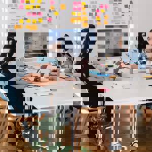 Five people in a meeting around a table all looking toward the screen that is on the table. Behind that screen are post-its on the wall.