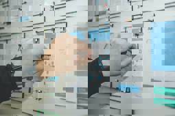 On a whiteboard there are some printed out documents, and a person is connecting lines between them by using a wire.