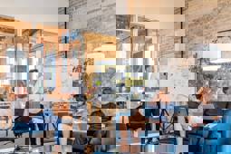 A presenter stands in front of a whiteboard on which a table has been drawn and post-its have been added into some cells. In the picture, three others are listening intently.